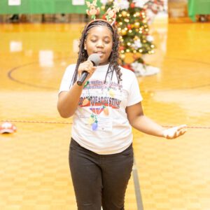 child with microphone in gymnasium with Christmas tree