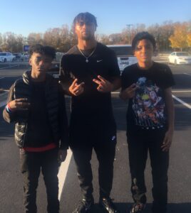 Three boys posing for a picture in a parking lot.