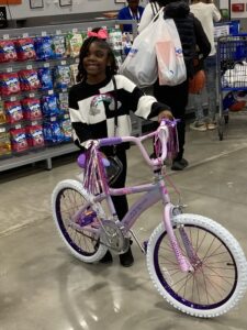 A young girl standing next to a purple bike in a store.