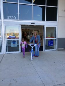 A woman and child standing in front of a store with a bicycle.