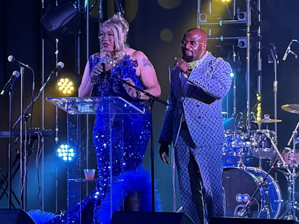 Two performers speaking at microphone on stage