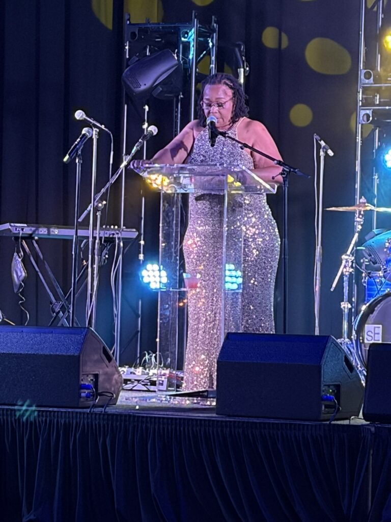 Woman in sequined gown speaking at podium